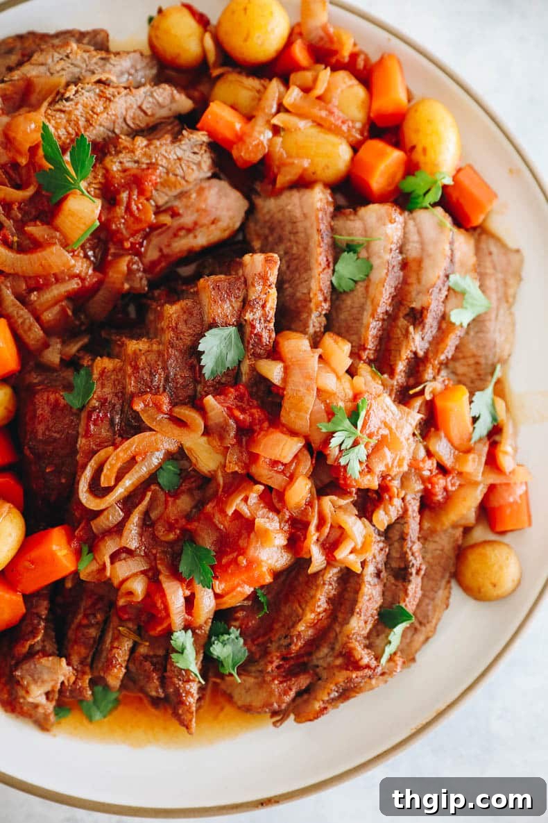 Perfectly Tender Smoked Brisket 10 Beautifully sliced brisket on a white platter, generously covered with its rich gravy, accompanied by tender potatoes, carrots, and a garnish of fresh parsley.