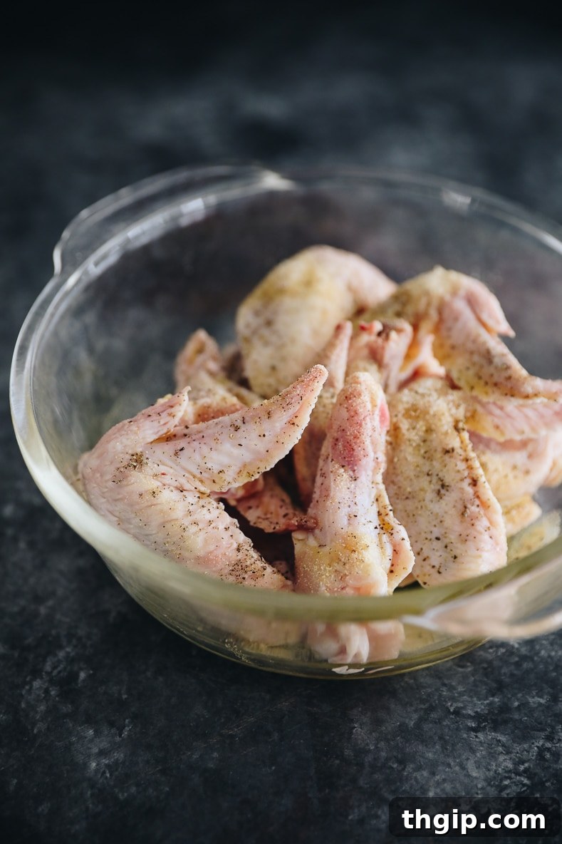 Fırında Sriracha Limonlu Tavuk Kanatları 3 Seasoned raw chicken wings on a baking sheet lined with parchment paper