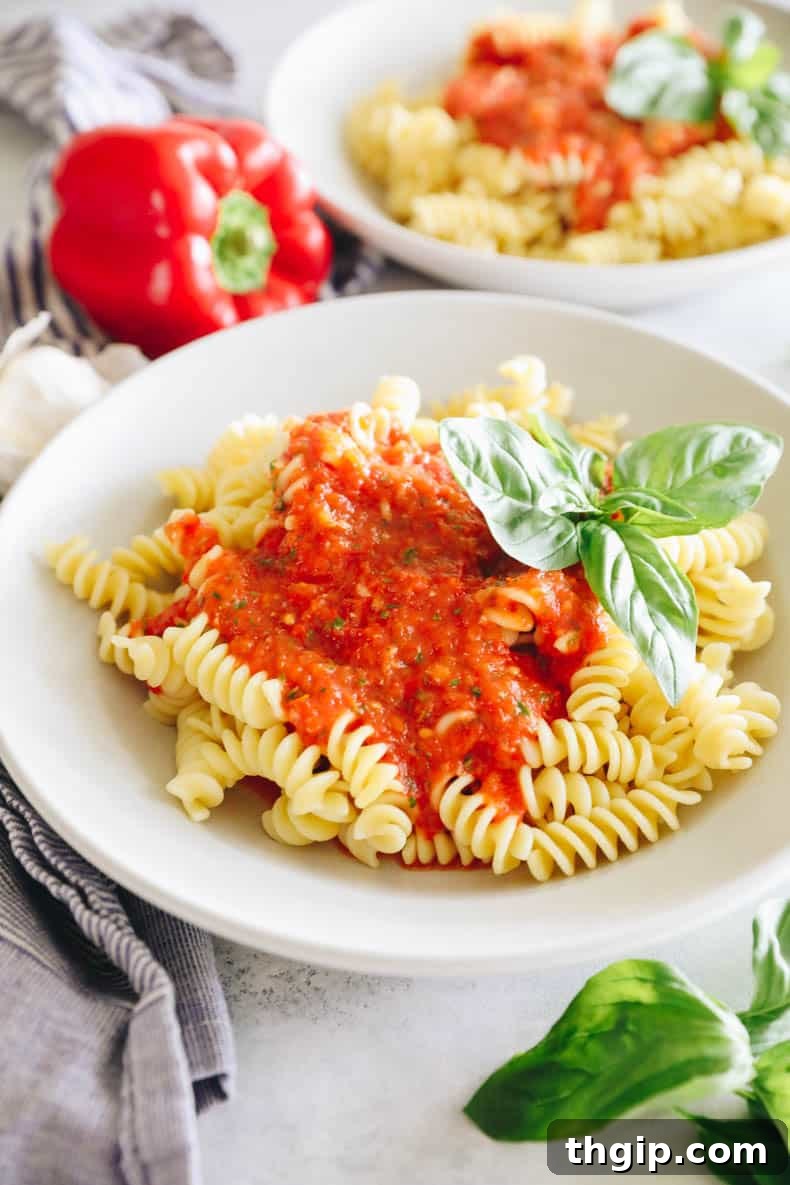 Flame-Kissed Red Pepper Spread 2 roasted red pepper sauce over fusilli in white shallow bowl with basil.