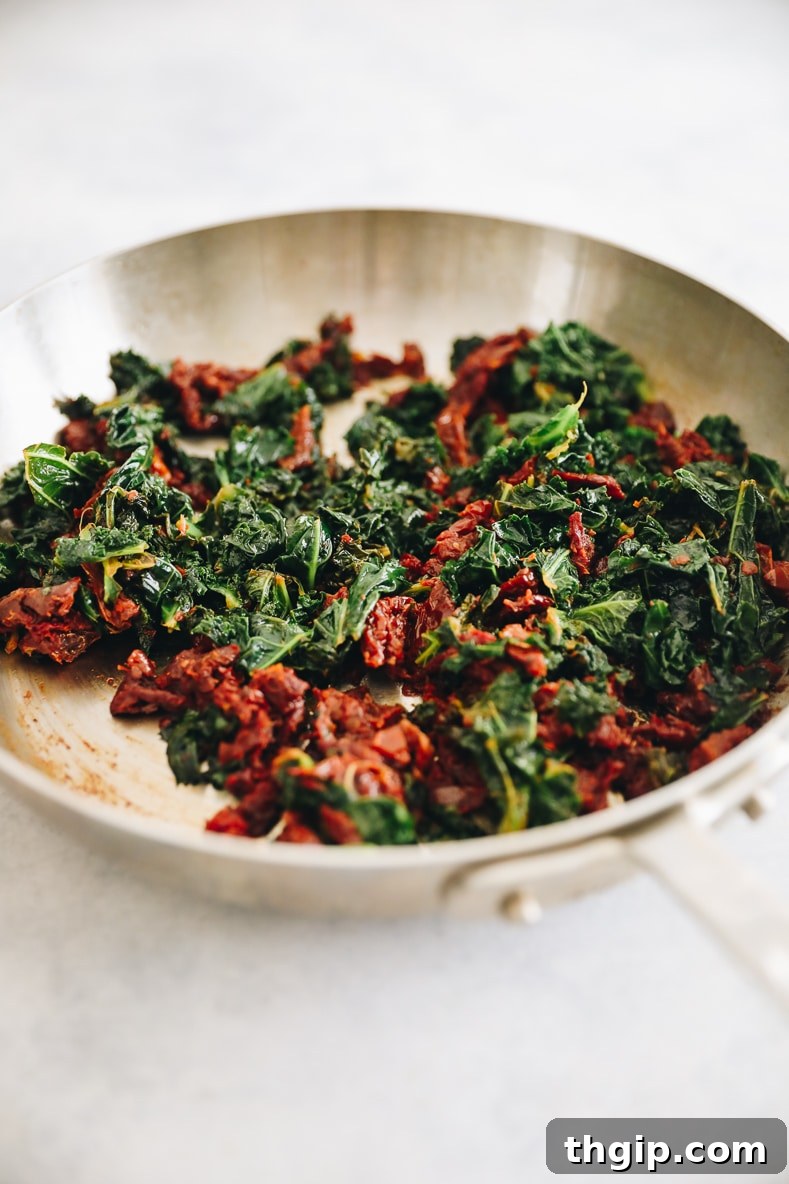 Wilted kale and chopped sundried tomatoes cooking in a pan.