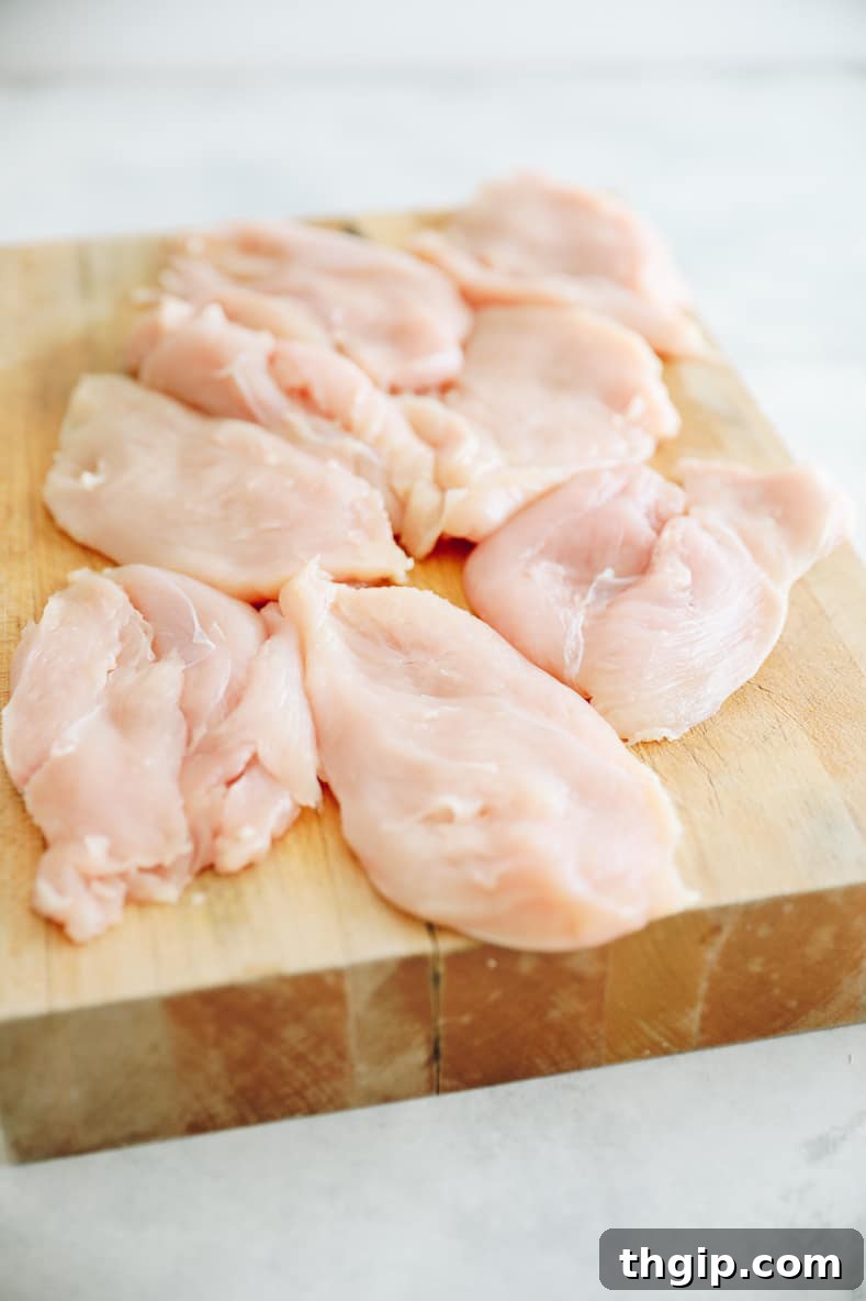 A chicken breast being pounded thin with a meat mallet between two sheets of parchment paper.