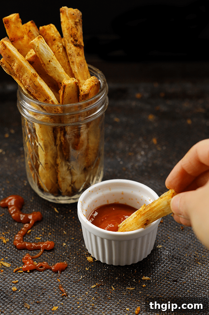 Crispy Baked Yuca Fries served with a bowl of green dipping sauce on a wooden board.