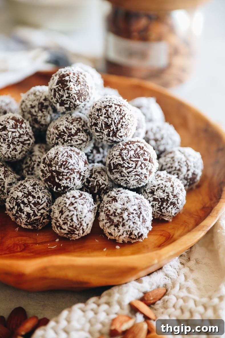 Coconut Almond Bliss Bites 2 Almond joy energy balls stacked on a wooden platter. Cream towel with almonds scattered in the foreground.