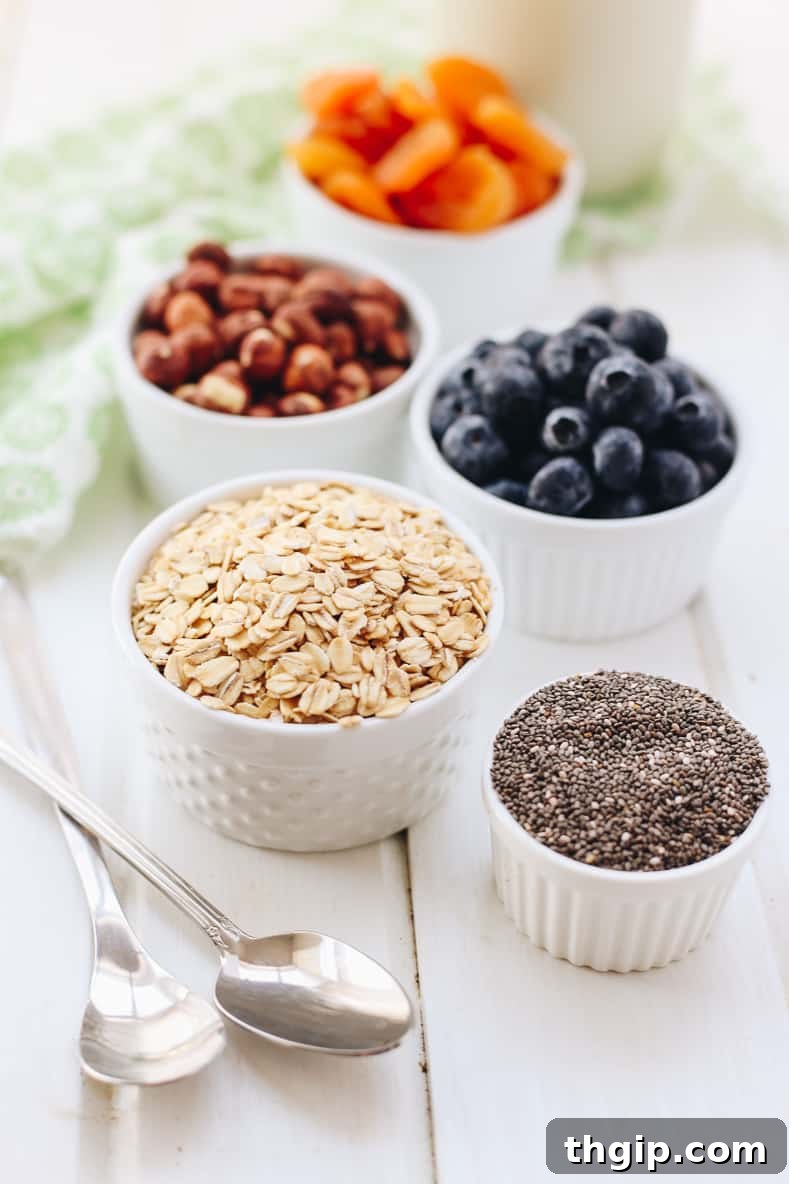 The second step in making Bircher Muesli: a mason jar filled with a mixture of rolled oats, chia seeds, chopped dried apricots, hazelnuts, and blueberries, before liquid is added.