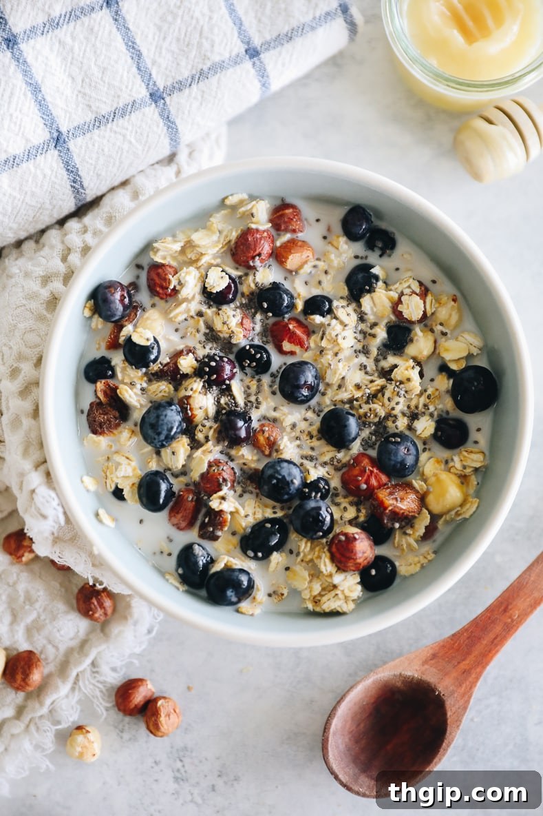 A close-up shot of the finished Bircher Muesli in a bowl, topped generously with fresh blueberries, chopped nuts, and a light drizzle, showcasing its creamy texture and vibrant toppings.