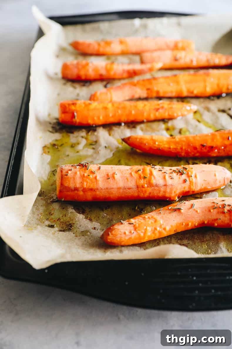 Velvety Ginger Carrot Sunshine 3 Close-up of roasted carrots seasoned with salt and fresh rosemary on a parchment-lined sheet pan.