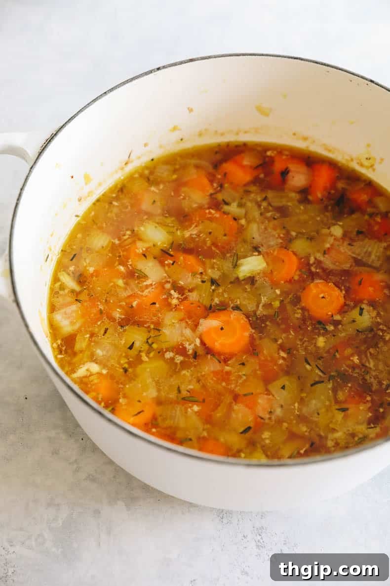 Velvety Ginger Carrot Sunshine 5 A large pot of simmering ginger carrot soup, with roasted carrots, vegetables, and vegetable stock creating a rich base.