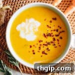 close-up image of creamy ginger carrot soup recipe in a white and blue bowl with coconut milk and red pepper flakes