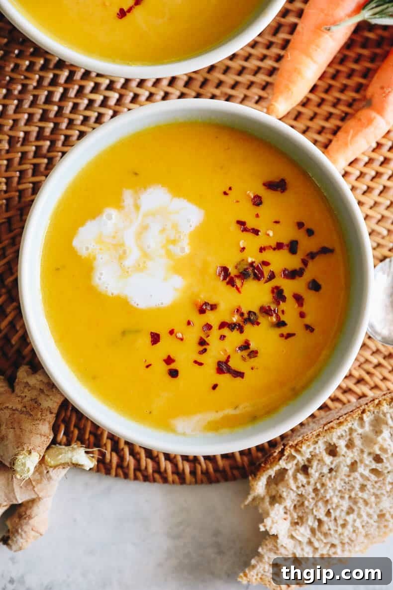 Velvety Ginger Carrot Sunshine 9 Overhead view of a comforting bowl of ginger carrot soup, beautifully topped with red pepper flakes and a decorative swirl of coconut cream.