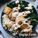 A vibrant and healthy Buddha Bowl, featuring brown rice, crispy tofu, steamed broccoli, and fresh kale, drizzled with a rich peanut sauce.