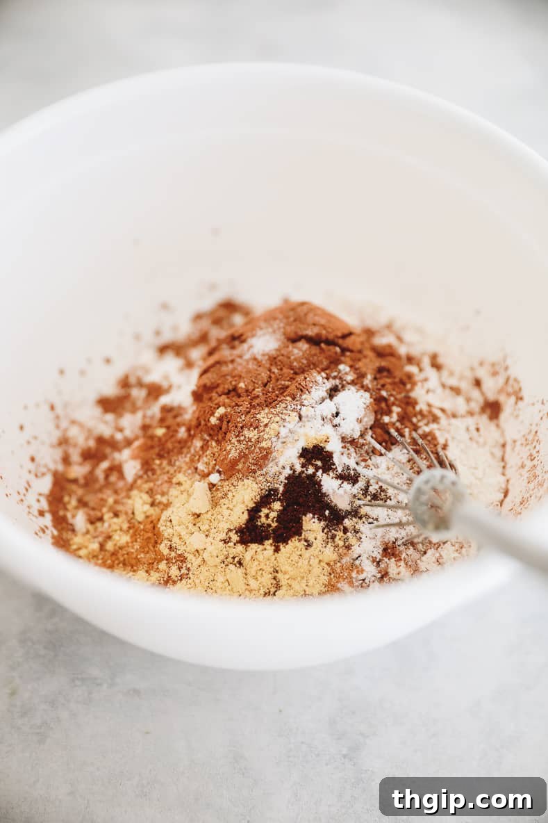 Spiced Chocolate Gingerbread Muffins 3 White mixing bowl containing dry ingredients for chocolate gingerbread muffins, with a whisk inside, ready for mixing.