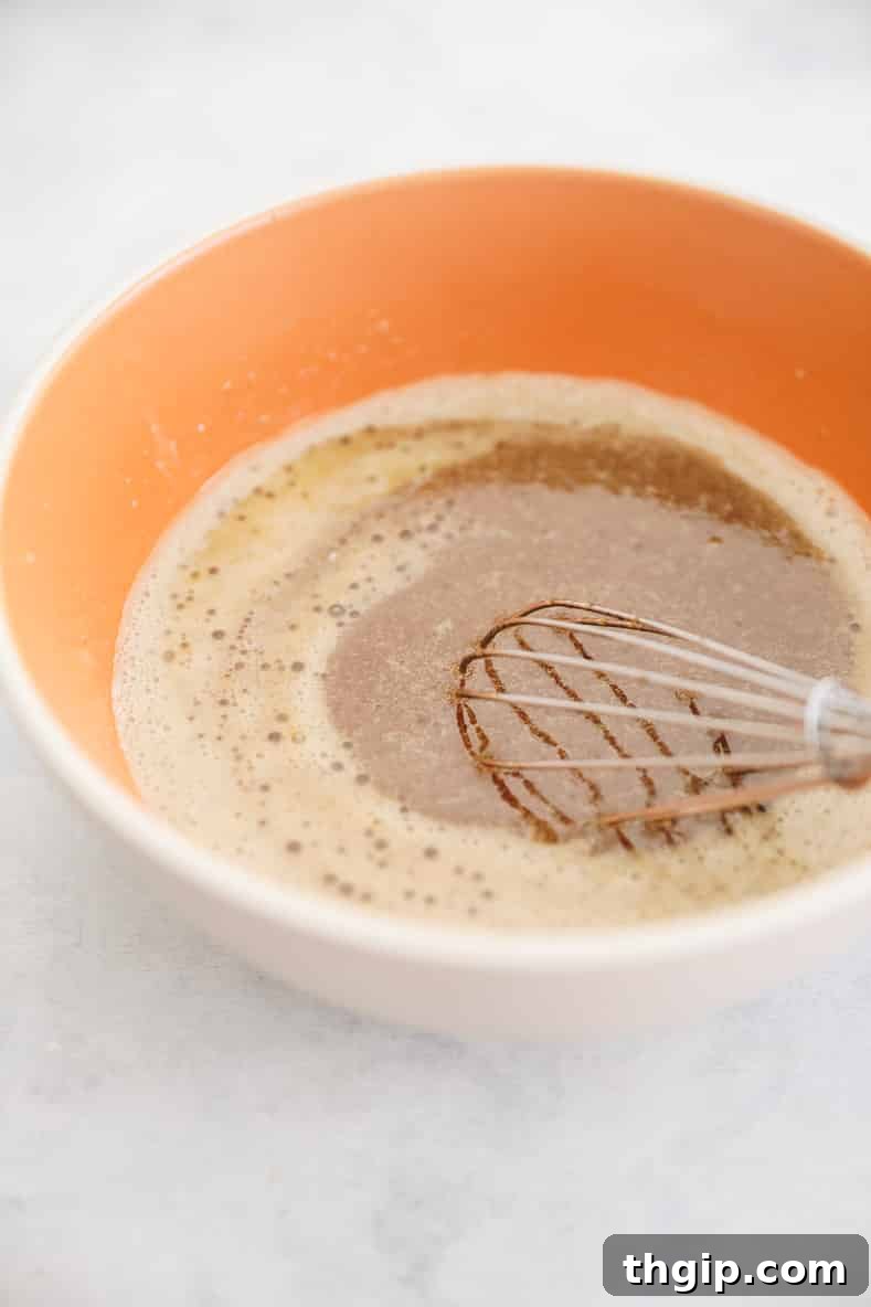 Spiced Chocolate Gingerbread Muffins 5 Orange bowl with a whisk in the combined wet ingredients, including applesauce, oil, syrup, molasses, milk, and egg, ready for dry ingredients.