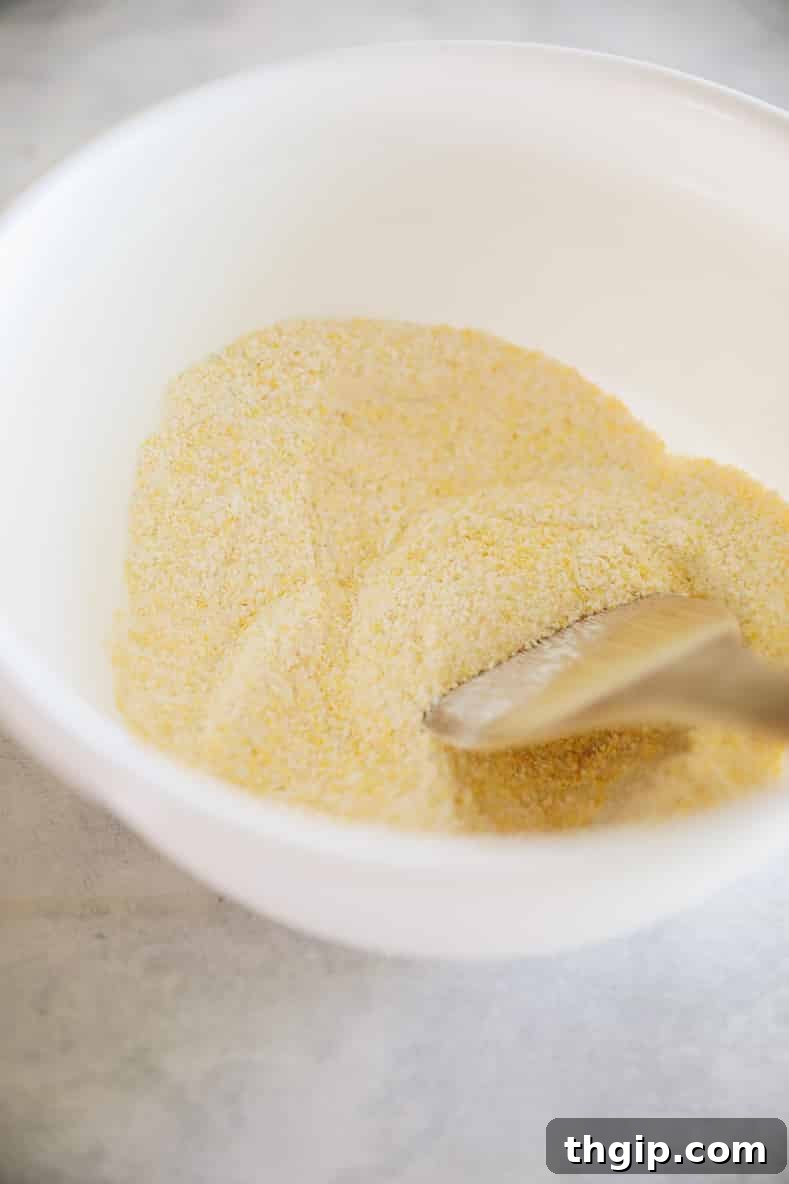 Dry ingredients for corn pancakes in a white mixing bowl with wooden spoon.