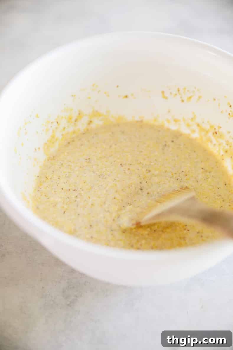 Corn pancake batter in a white mixing bowl with a wooden spoon.