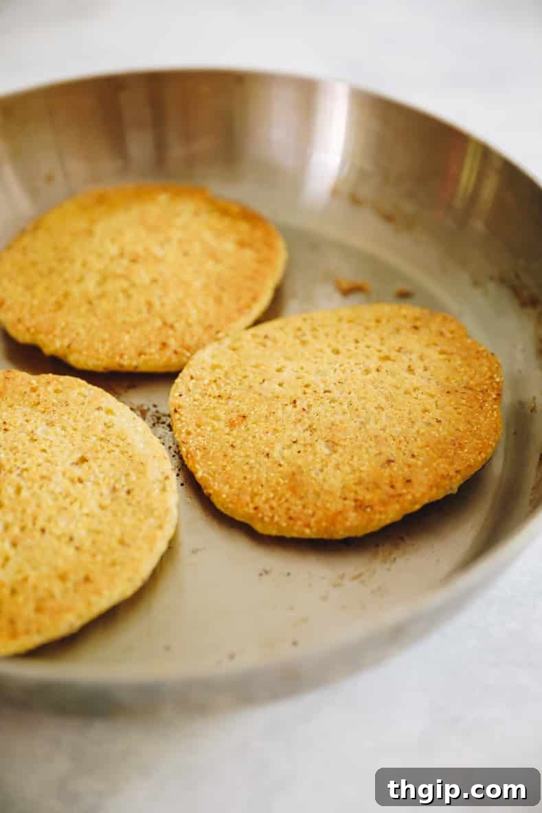 Three cooked corn pancakes in a sauté pan.